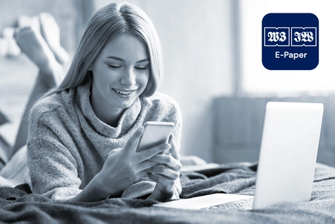 Eine Frau, die im Bett liegt und auf ihr Handy schaut. Neben ihr steht ein Laptop